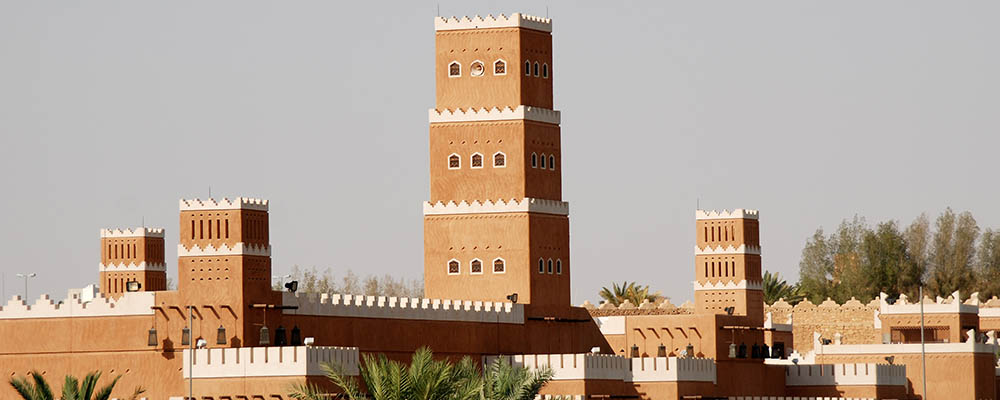Najran Fort with its traditional mud-brick architecture, surrounded by palm trees and desert landscape under a clear blue sky